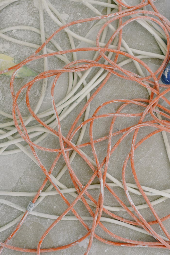 Long thing snaking white and orange messy wires on even gray dirty floor in daytime